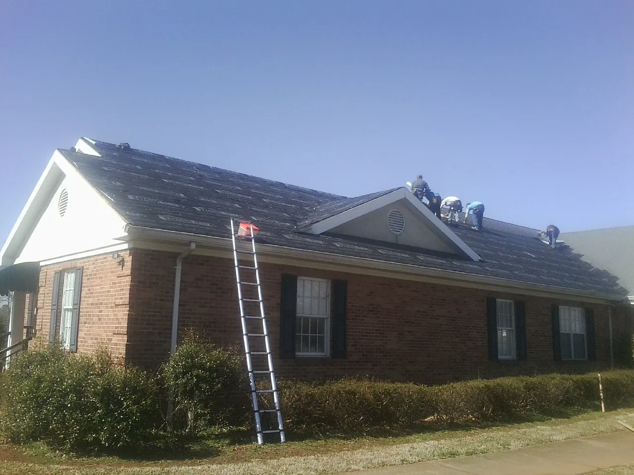 Crew tearing shingles off a brick ranch roof with a ladder set — Emergency Roof Repair work by our crew in Granville