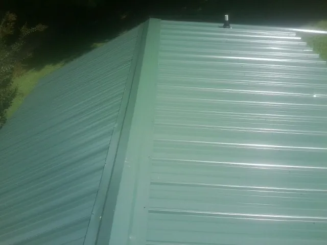 New green metal panels meeting at the ridge of a roof — Flat Roof Repair work by our crew in Granville