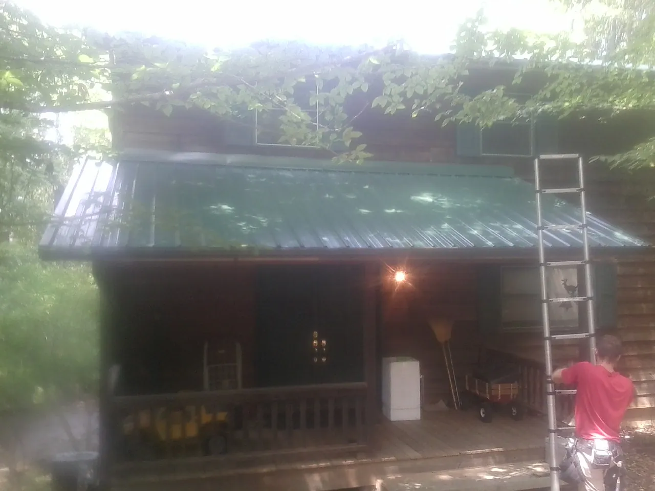 Worker on a ladder at the green porch roof of a wooded cabin in Granville