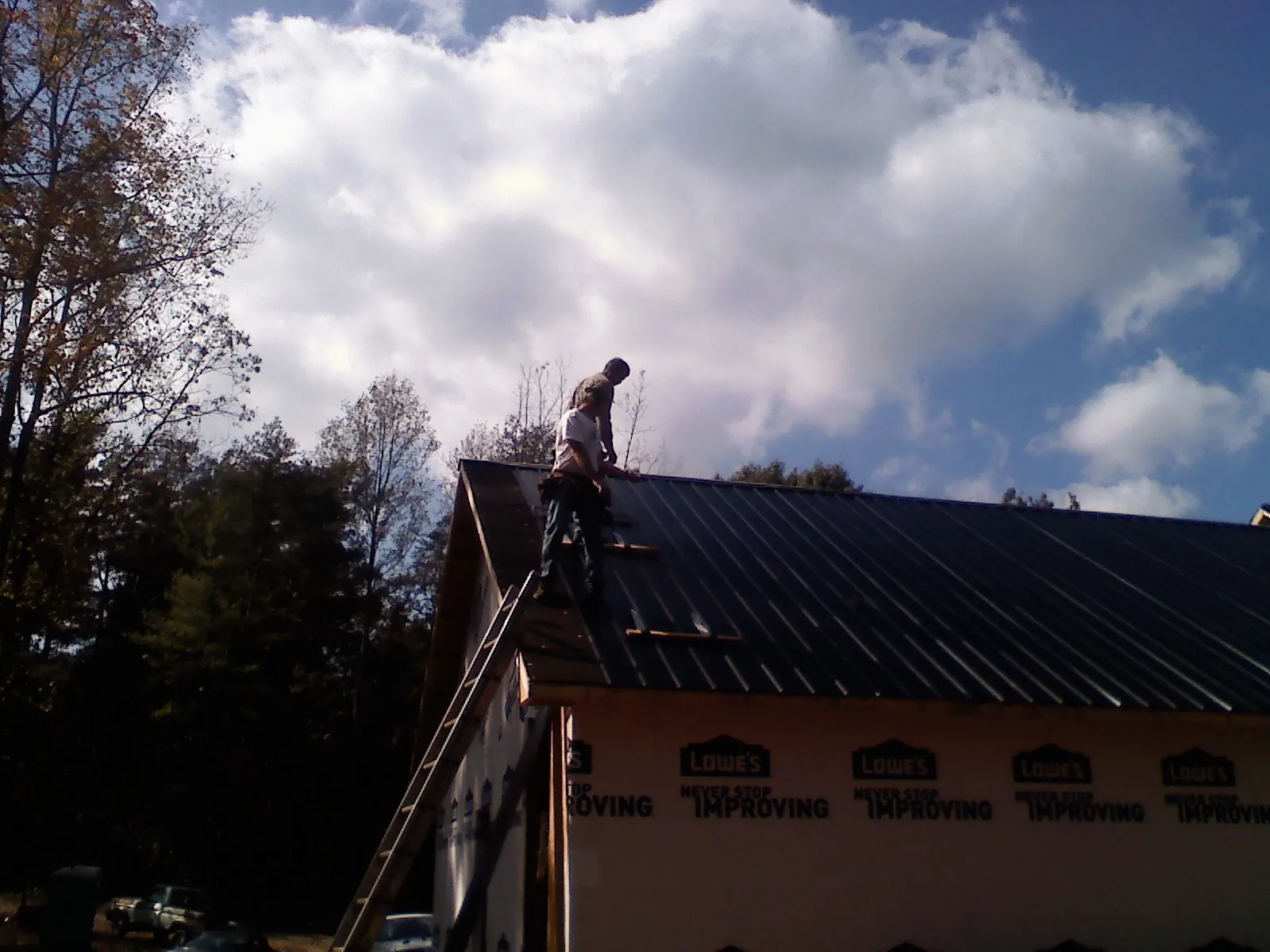 Roofer fastening dark metal panels high against a cloudy sky, from a Roof Inspection job in Granville